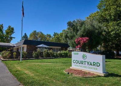 A grassy area and the welcome sign to Courtyard Healthcare Center