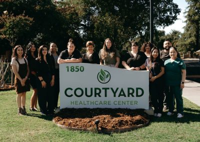 The administrative and care team at Courtyard Healthcare Center standing in front of a monument sign